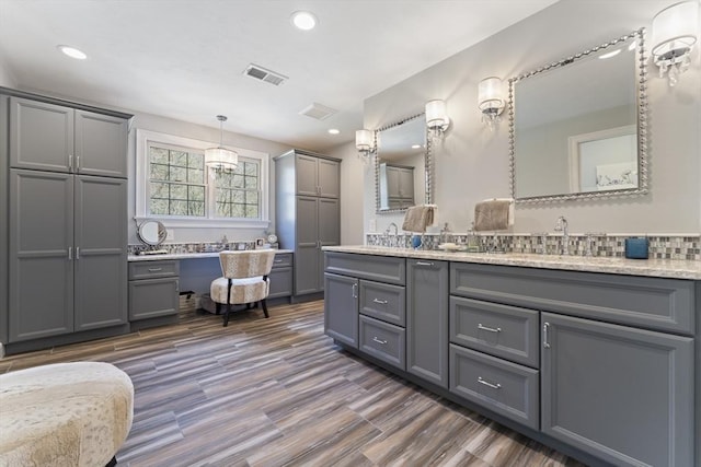 full bathroom with a sink, a bath, double vanity, visible vents, and wood finished floors