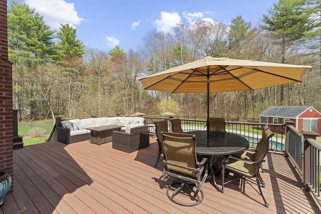 deck with an outdoor structure, a shed, outdoor dining area, a view of trees, and an outdoor living space