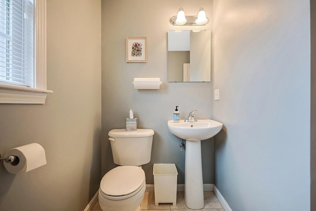 half bathroom with tile patterned flooring, toilet, baseboards, and a sink