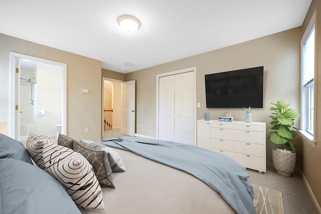 bedroom featuring a closet, baseboards, light colored carpet, and ensuite bath