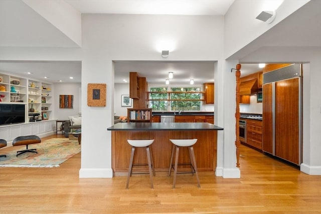 kitchen featuring stainless steel appliances, light wood-style flooring, dark countertops, and a breakfast bar area