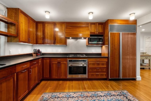 kitchen with appliances with stainless steel finishes, wood finished floors, premium range hood, and dark countertops
