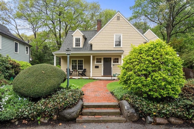 view of front of house with a porch, a chimney, and a shingled roof