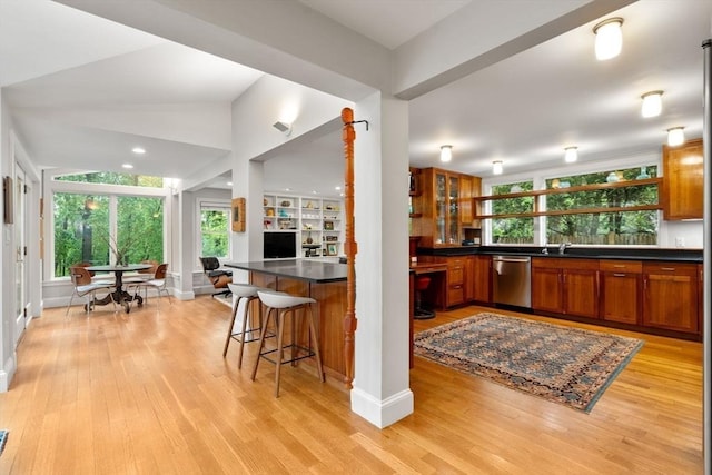 kitchen featuring dishwasher, brown cabinets, dark countertops, and light wood-style flooring