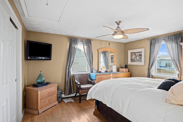 bedroom featuring ceiling fan, a closet, light hardwood / wood-style floors, and a baseboard heating unit