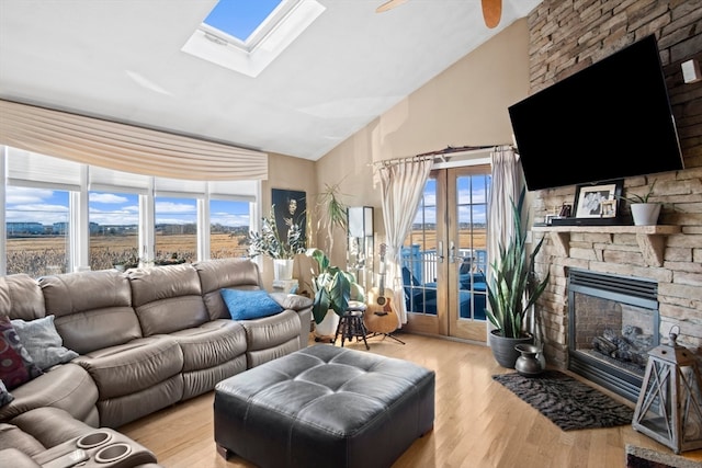 living room with french doors, a stone fireplace, a skylight, ceiling fan, and light wood-type flooring