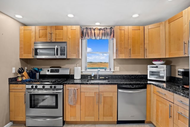 kitchen with light brown cabinetry, sink, appliances with stainless steel finishes, and dark stone counters