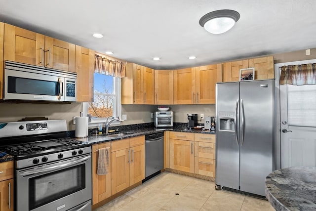 kitchen with dark stone counters, sink, light tile patterned floors, light brown cabinetry, and stainless steel appliances