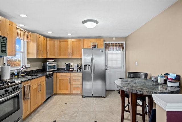 kitchen featuring appliances with stainless steel finishes, sink, light tile patterned floors, and dark stone countertops