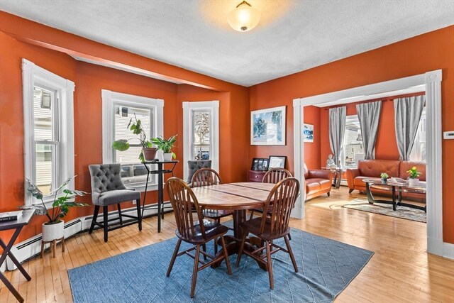 dining room with hardwood / wood-style floors, baseboard heating, and a textured ceiling