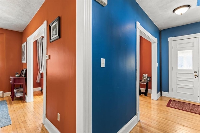 corridor with baseboards, light wood-type flooring, and a textured ceiling