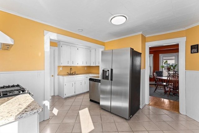 kitchen featuring a wainscoted wall, light tile patterned flooring, a sink, stainless steel appliances, and white cabinetry