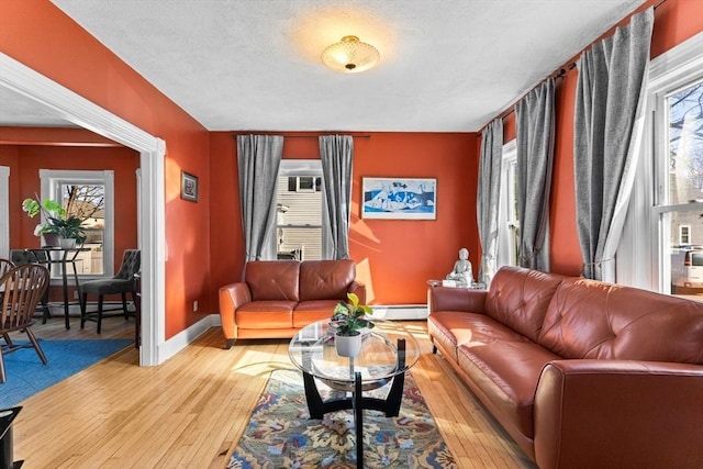 living area featuring light wood-style flooring, a textured ceiling, a baseboard heating unit, and baseboards