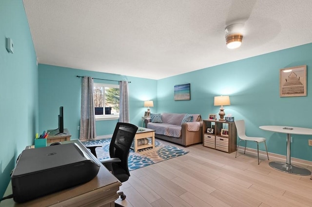 home office with light wood-type flooring, ceiling fan, and a textured ceiling