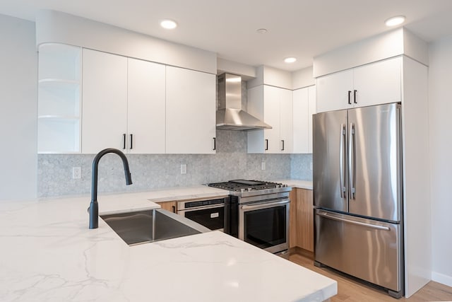 kitchen featuring light wood-type flooring, light stone counters, white cabinetry, wall chimney range hood, and appliances with stainless steel finishes