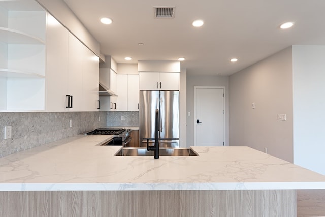 kitchen with appliances with stainless steel finishes, white cabinets, backsplash, kitchen peninsula, and light stone countertops