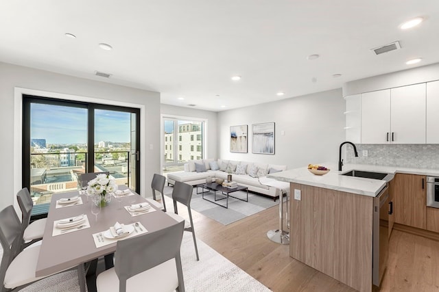 kitchen featuring light hardwood / wood-style floors, white cabinets, backsplash, stainless steel appliances, and sink