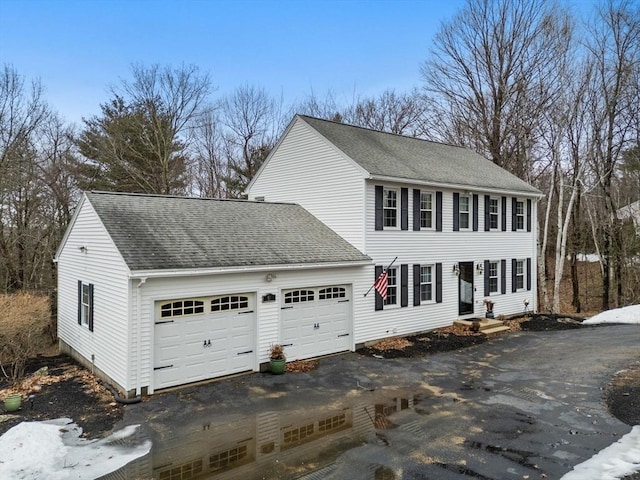 exterior space featuring driveway, an attached garage, and a shingled roof