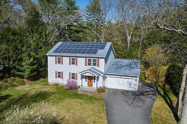 colonial inspired home featuring a garage, a front yard, a shingled roof, driveway, and solar panels