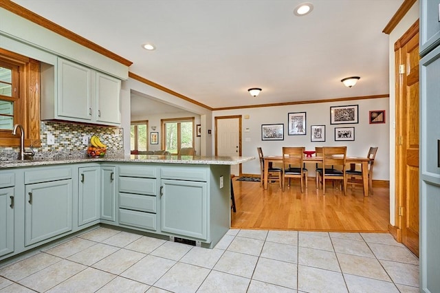 kitchen featuring crown molding, a sink, light tile patterned floors, light stone counters, and a peninsula