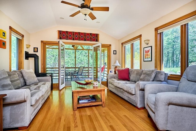 living room with light wood-style floors, ceiling fan, a wood stove, and lofted ceiling