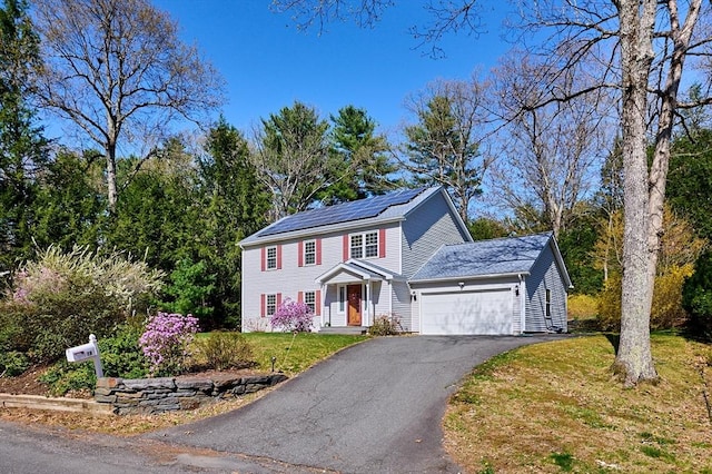 colonial house with a garage, a front lawn, solar panels, and driveway