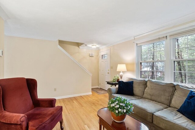 living area with crown molding, light wood-type flooring, baseboards, and stairs