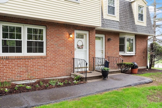 view of exterior entry featuring a shingled roof and brick siding
