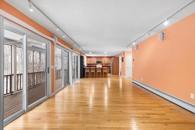 interior space with baseboard heating, ceiling fan, and light hardwood / wood-style flooring