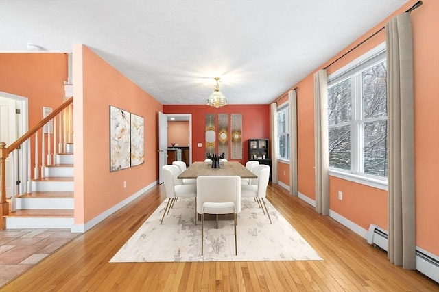 dining space featuring a healthy amount of sunlight, light wood-type flooring, a baseboard radiator, and a notable chandelier