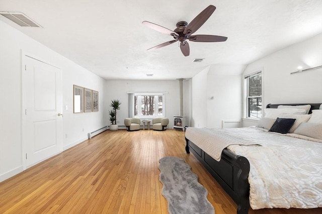 bedroom featuring vaulted ceiling, ceiling fan, a baseboard radiator, light hardwood / wood-style floors, and a wood stove