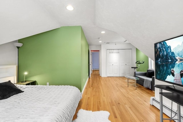 bedroom featuring hardwood / wood-style flooring, vaulted ceiling, a closet, and a baseboard heating unit