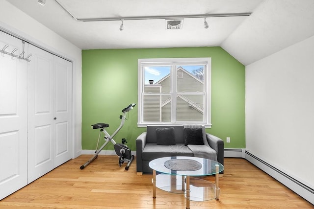 living area with vaulted ceiling, a baseboard radiator, track lighting, and light wood-type flooring