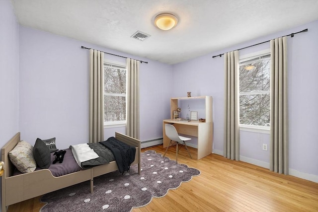 bedroom featuring multiple windows, light hardwood / wood-style floors, and a baseboard heating unit