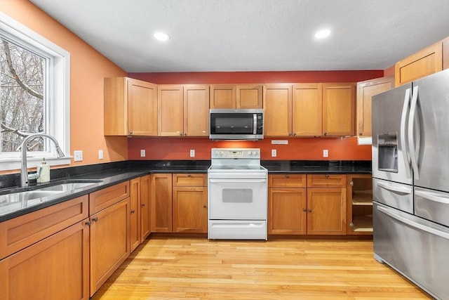 kitchen with dark stone counters, sink, appliances with stainless steel finishes, and light hardwood / wood-style flooring