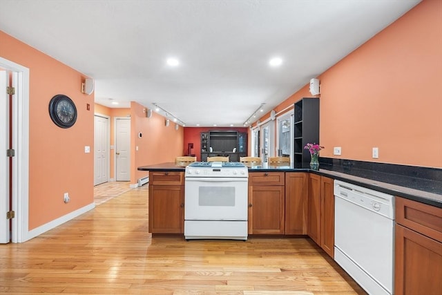 kitchen featuring white appliances, dark stone counters, track lighting, light hardwood / wood-style floors, and kitchen peninsula