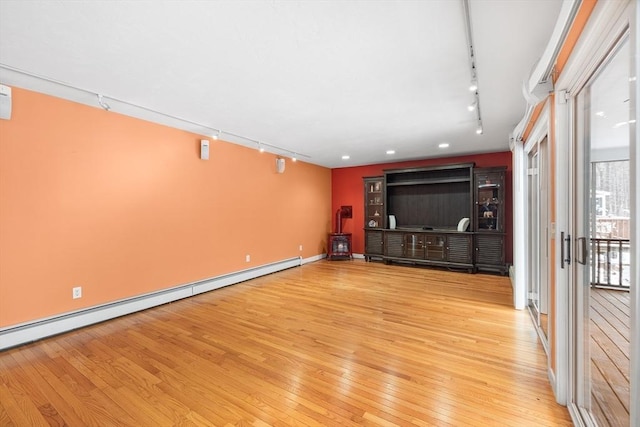 unfurnished living room featuring baseboard heating, rail lighting, and light hardwood / wood-style floors