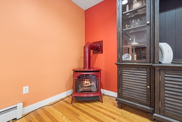 living area with hardwood / wood-style floors, a wood stove, baseboard heating, and vaulted ceiling