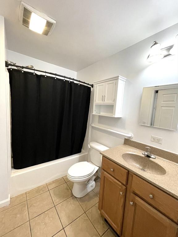 full bathroom with shower / bath combo with shower curtain, tile patterned floors, toilet, and vanity