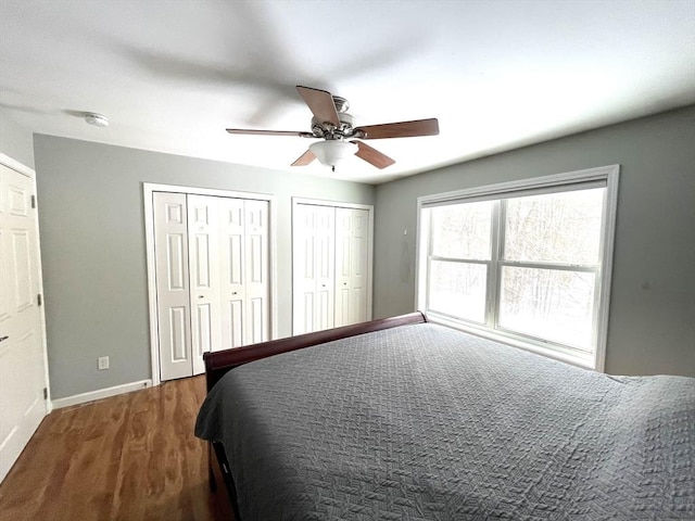 bedroom with two closets, dark wood-type flooring, and ceiling fan