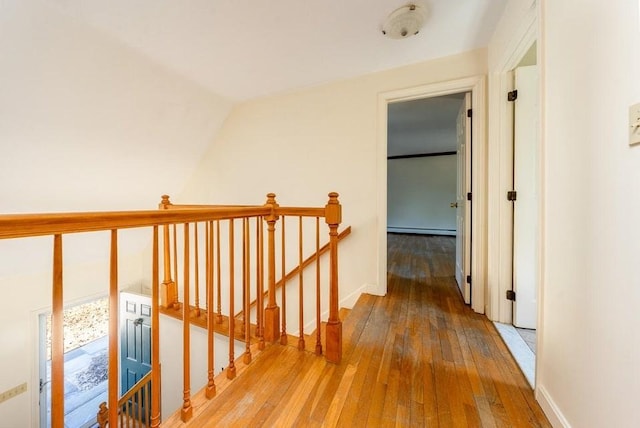 hall with hardwood / wood-style floors, baseboard heating, and an upstairs landing