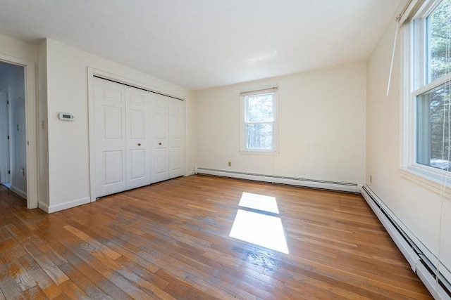 unfurnished bedroom featuring a baseboard radiator, baseboards, baseboard heating, and hardwood / wood-style floors