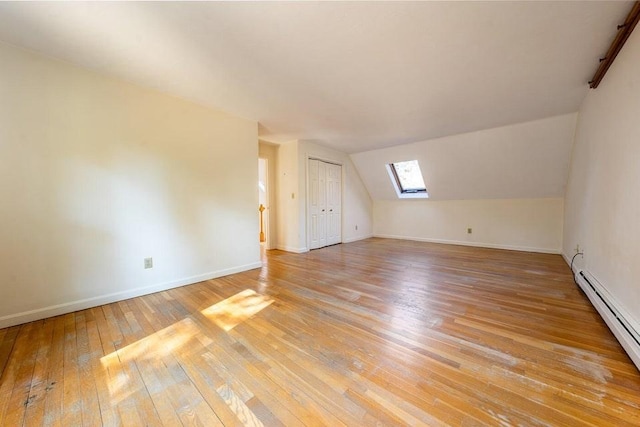 bonus room featuring light wood-type flooring, lofted ceiling with skylight, baseboards, and baseboard heating