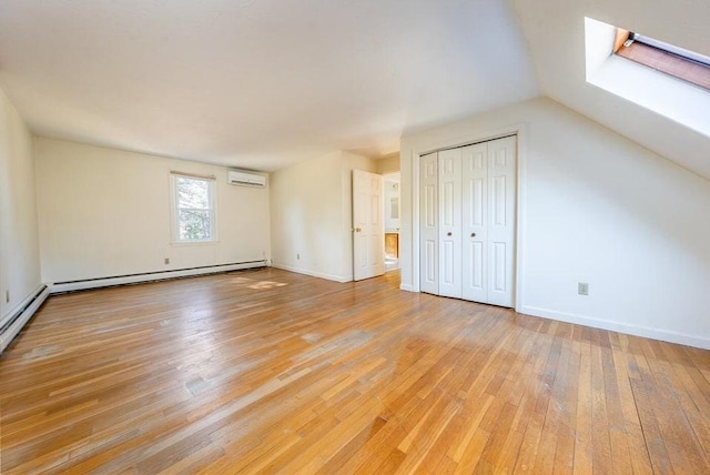 additional living space with a skylight, baseboards, a wall unit AC, baseboard heating, and light wood-type flooring