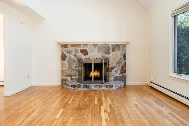 details with a baseboard heating unit, a stone fireplace, baseboards, and wood finished floors