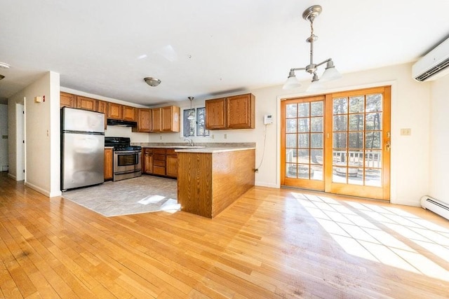 kitchen featuring a wall mounted AC, appliances with stainless steel finishes, brown cabinetry, light wood-style floors, and under cabinet range hood