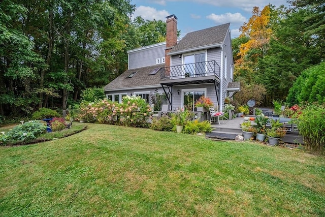 rear view of property with a patio, a balcony, a lawn, a chimney, and roof with shingles
