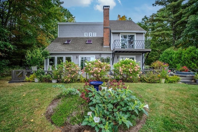 rear view of property featuring a lawn, roof with shingles, a chimney, and a balcony