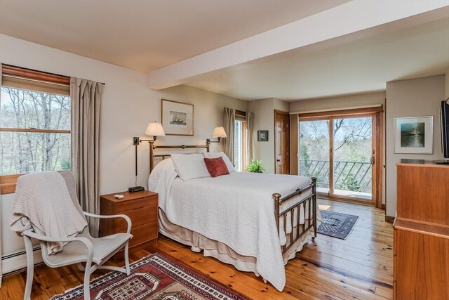 bedroom with a baseboard heating unit, light wood finished floors, and access to exterior