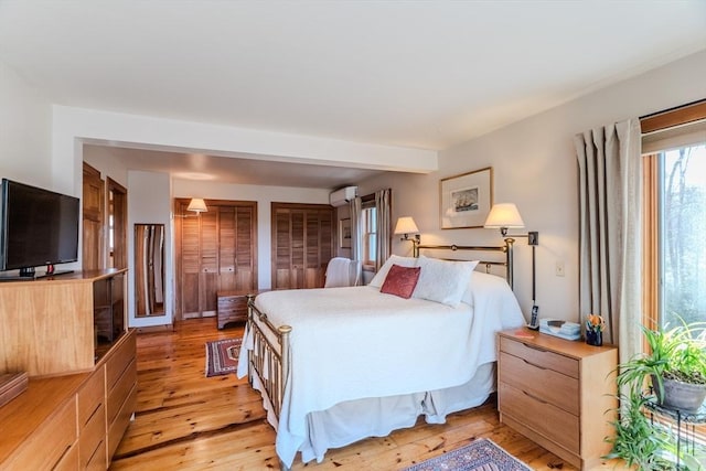 bedroom with a wall mounted air conditioner, two closets, and light wood-type flooring